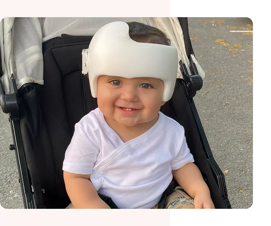 Baby wearing a helmet smiling in a stroller